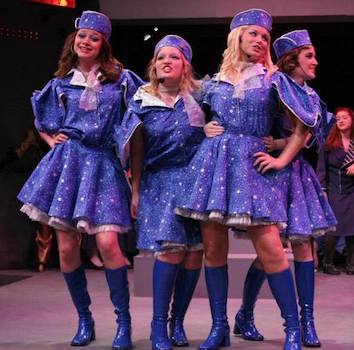 A group of girls onstage wearing blue sparkling dresses 