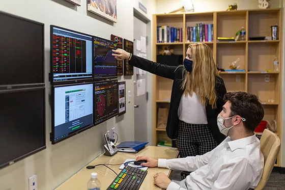 Students point at computer monitors with financial data