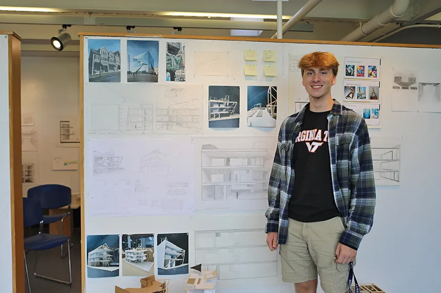A student standing by their work pinned on a gallery wall