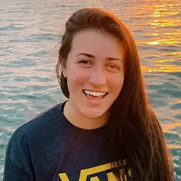 Student smiles by the water at sunset wearing a Vans T-shirt.