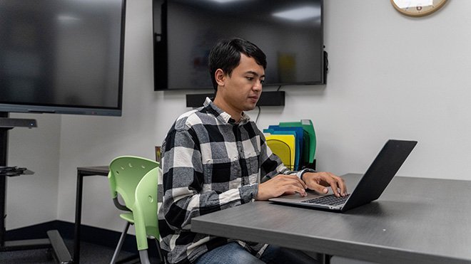 Kyle Villella ’23 sits at a desk and looks at his laptop in the Education Department's model classroom