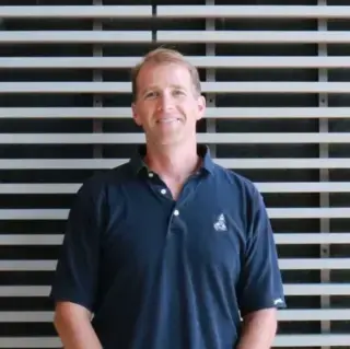 Portrait of Brian Wysor, man standing against wall with blue shirt.