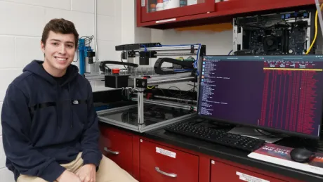 Colton Pelletier proudly sits next to his robotic creation in the lab.