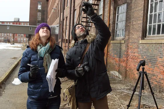 Roger Williams University Historic Preservation students stand using a camera to examine a historic building