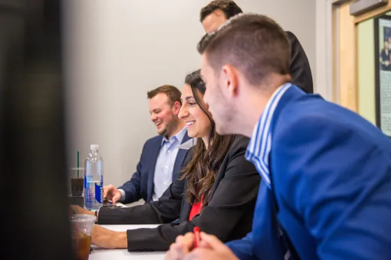 Roger Williams University business students look in on a project on a computer