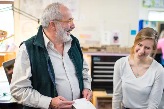 A faculty member stands laughing with a student