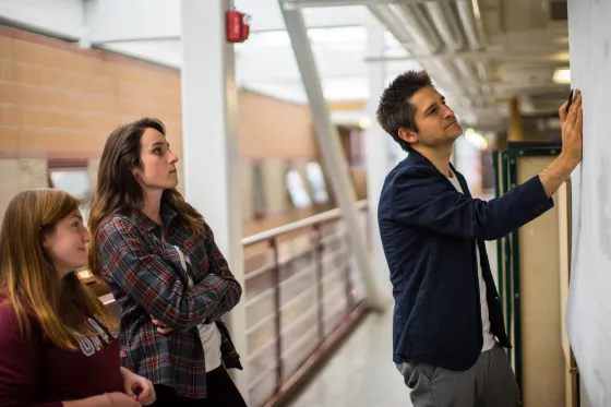 A professor stands working on an architectural drawing with students