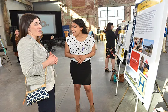 A student smiles and laughs while presenting research to a staff member