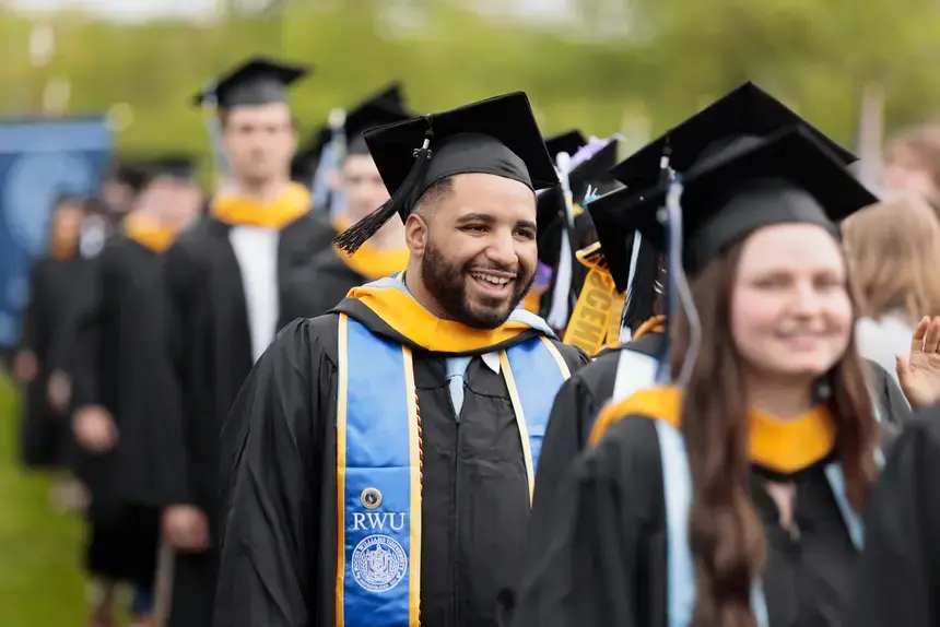 Graduate student in commencement regalia walking in the 2025 ceremony.