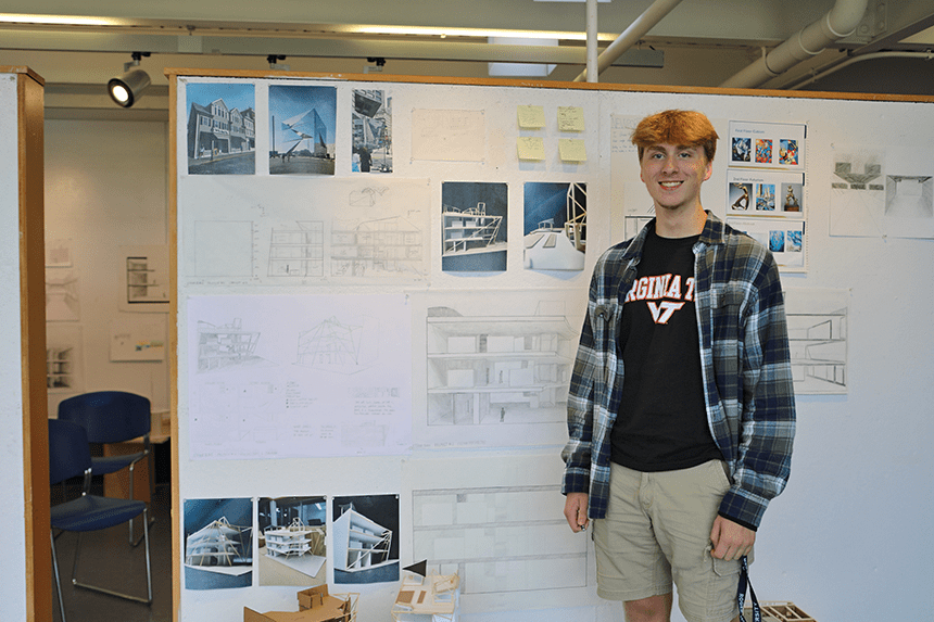 A student standing by their work pinned on a gallery wall 