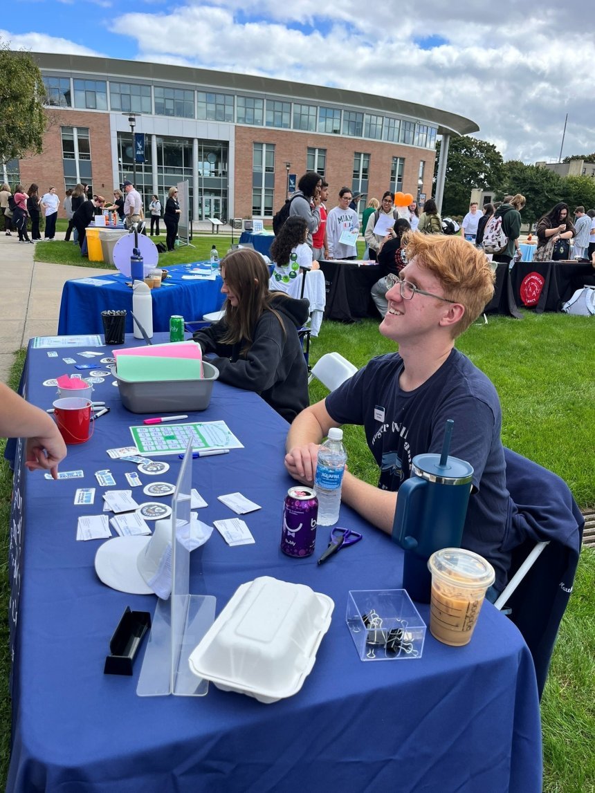 two peer mentors sitting at table outside talking to another campus community member