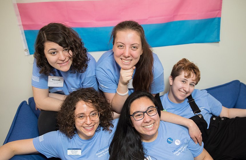 QTRAC students and staff sitting on a couch in front of a trans pride flag.