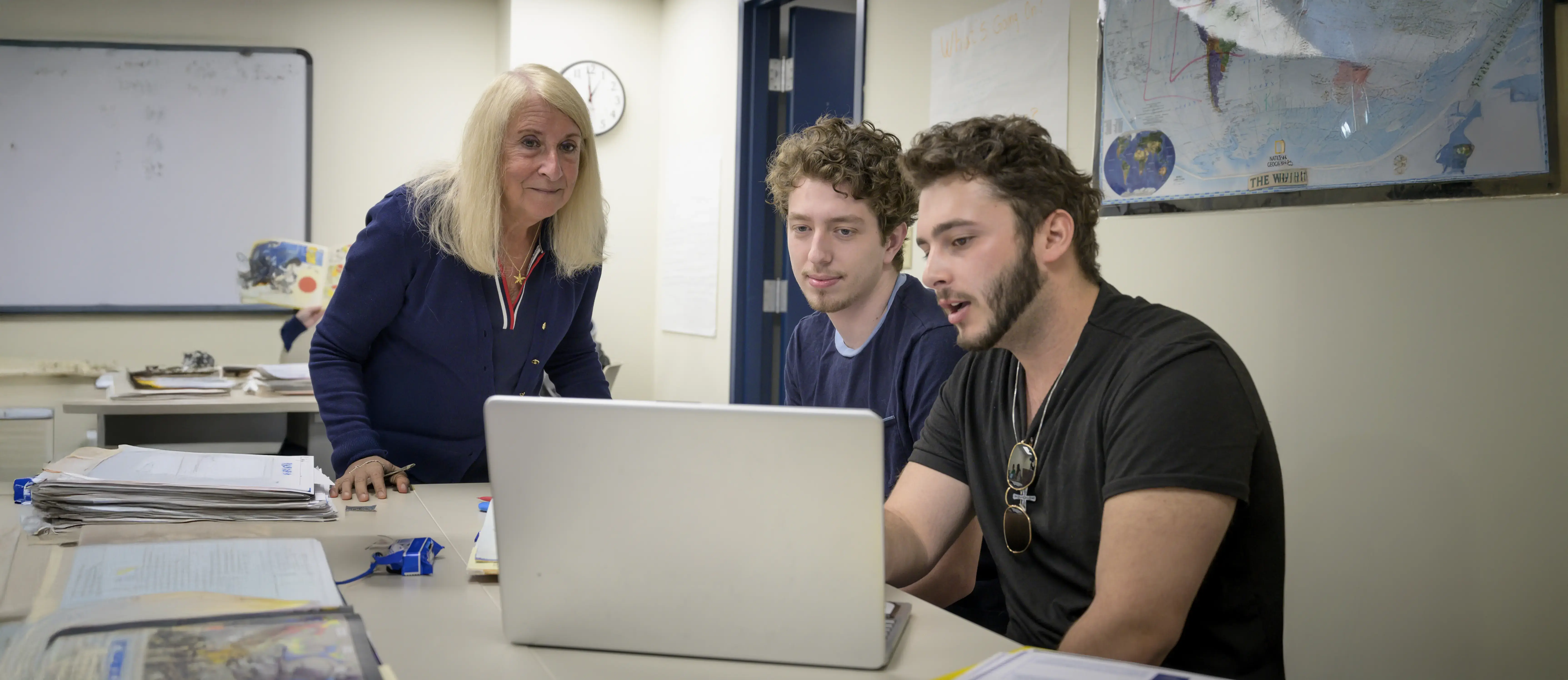 Two Education students showing something on a laptop to their instructor, who is leaning in and observing attentively.
