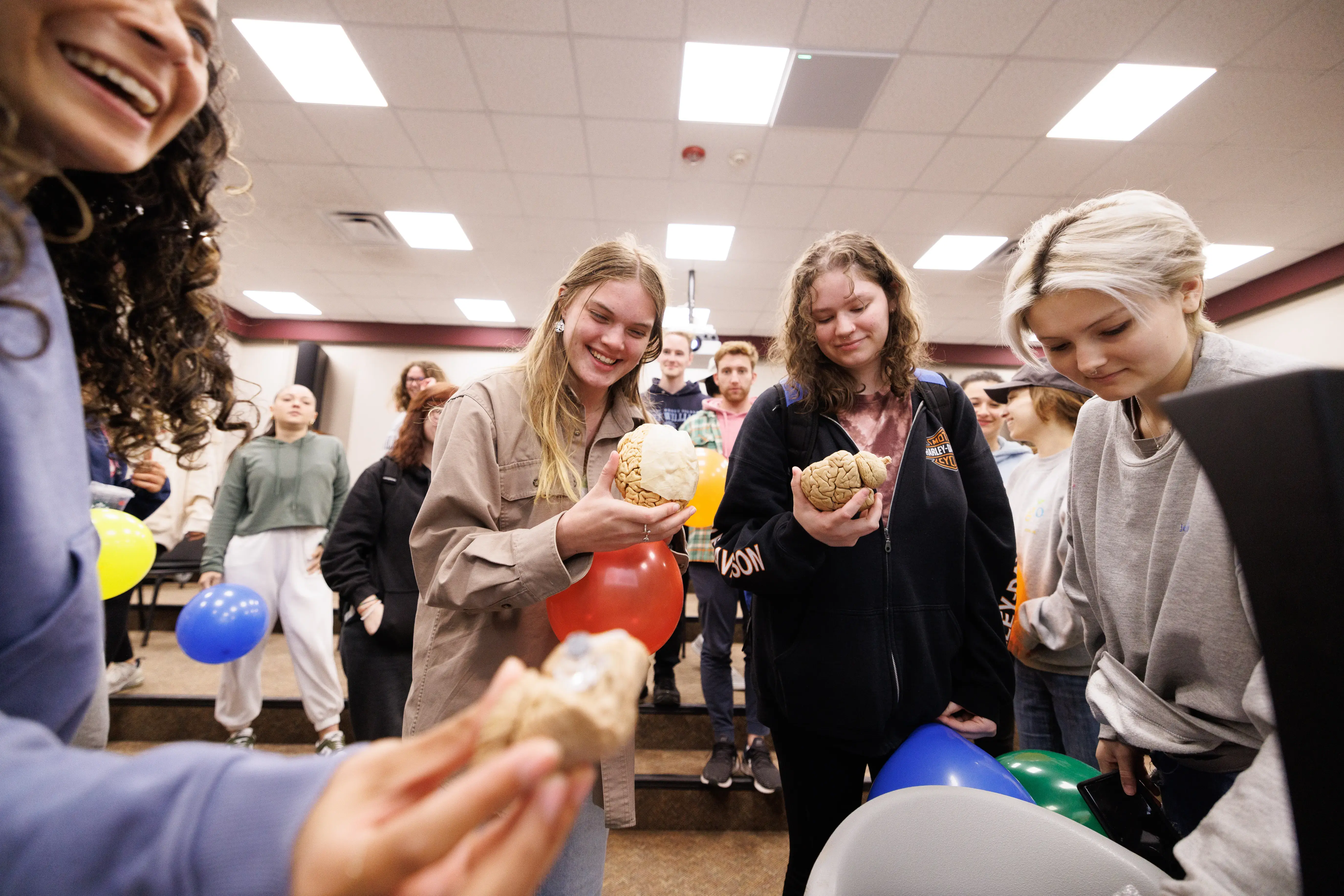 Students smile and examine brain models while holding balloons during a classroom activity or event.