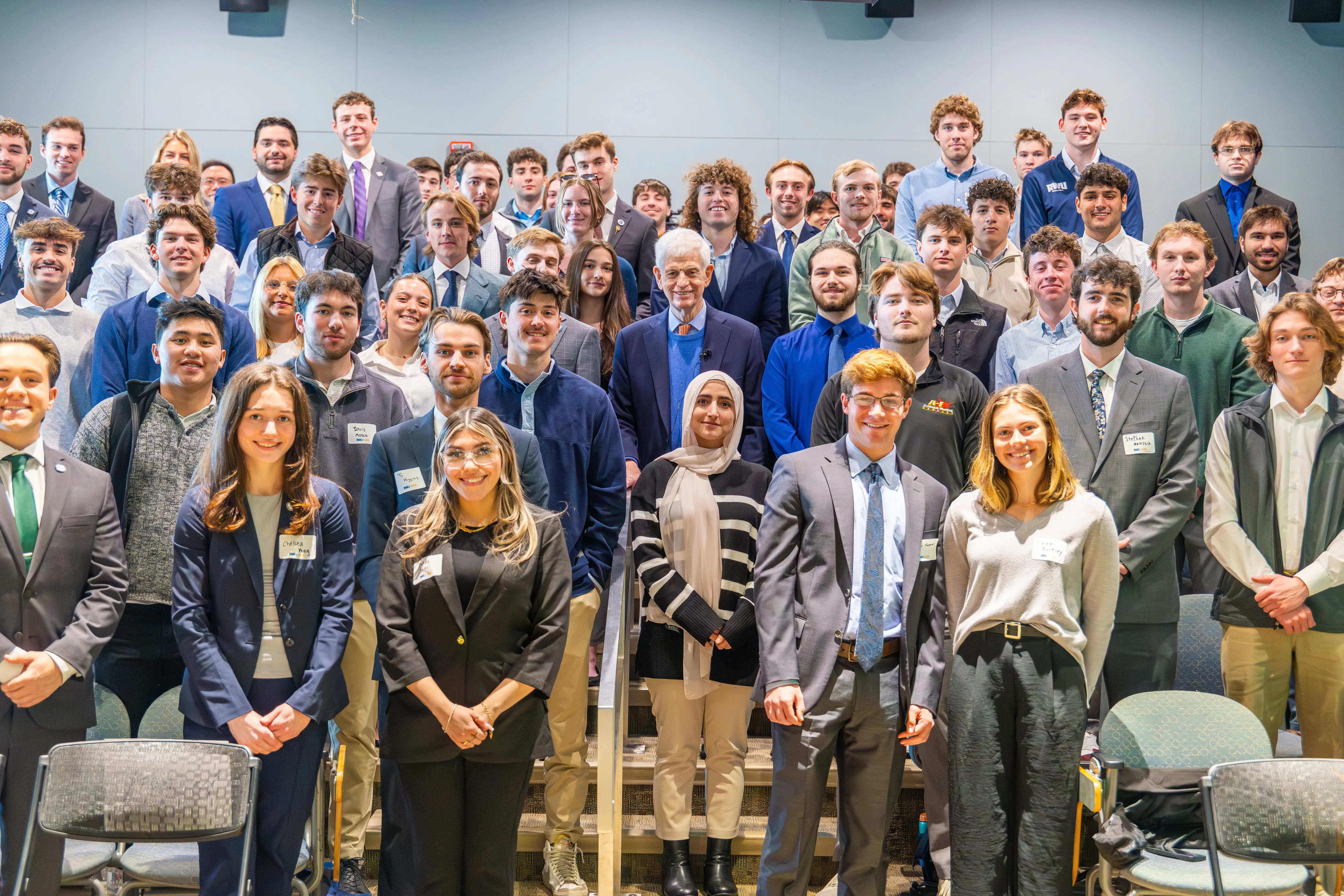 Large group of professionally dressed students pose together indoors on a staircase.
