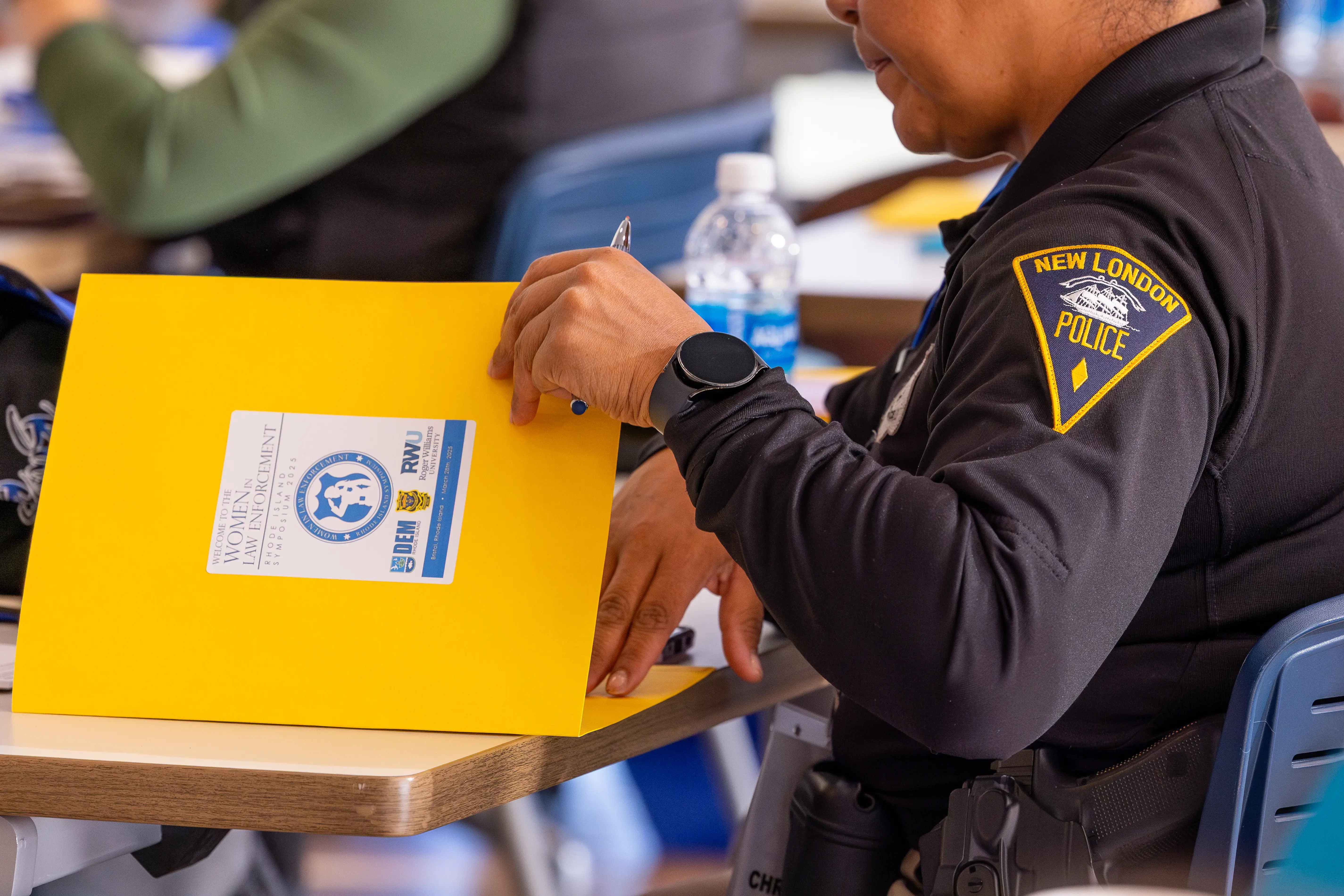 A New London police officer holds a “Women in Law Enforcement” folder at a table during a training or conference.