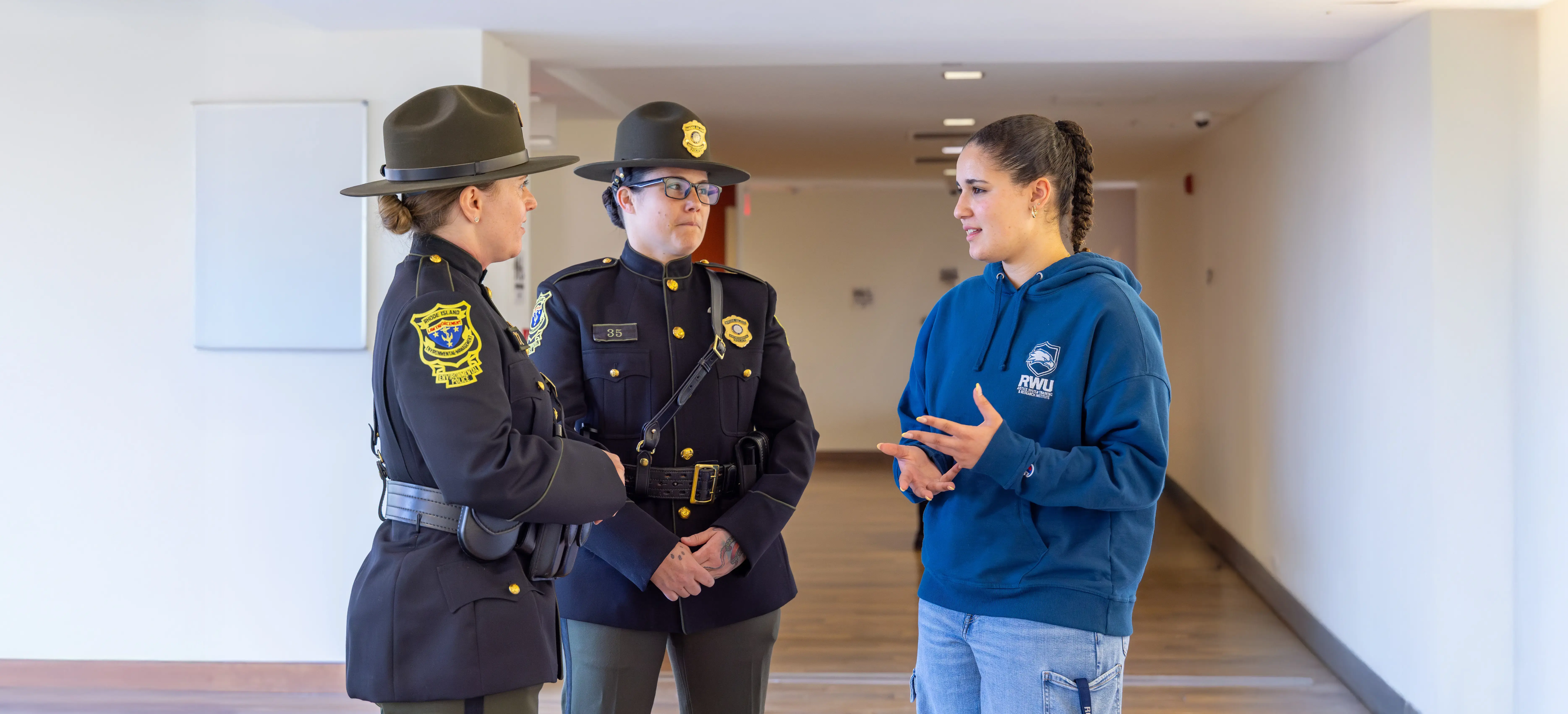 A Security Assurance Studies student receives career advice from two uniformed law enforcement professionals in a hallway.