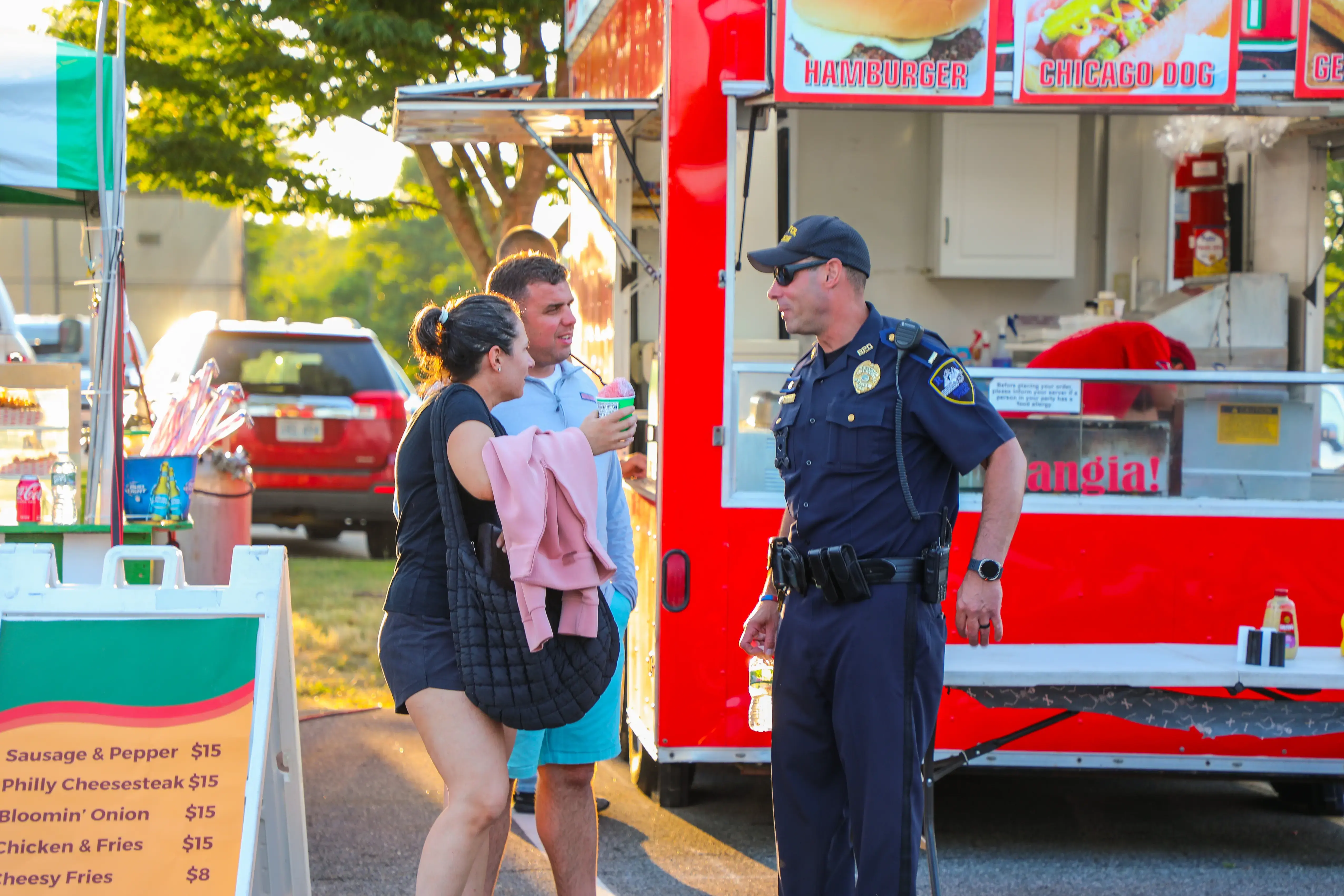 A police officer talks with two people near a red food truck at a community event.