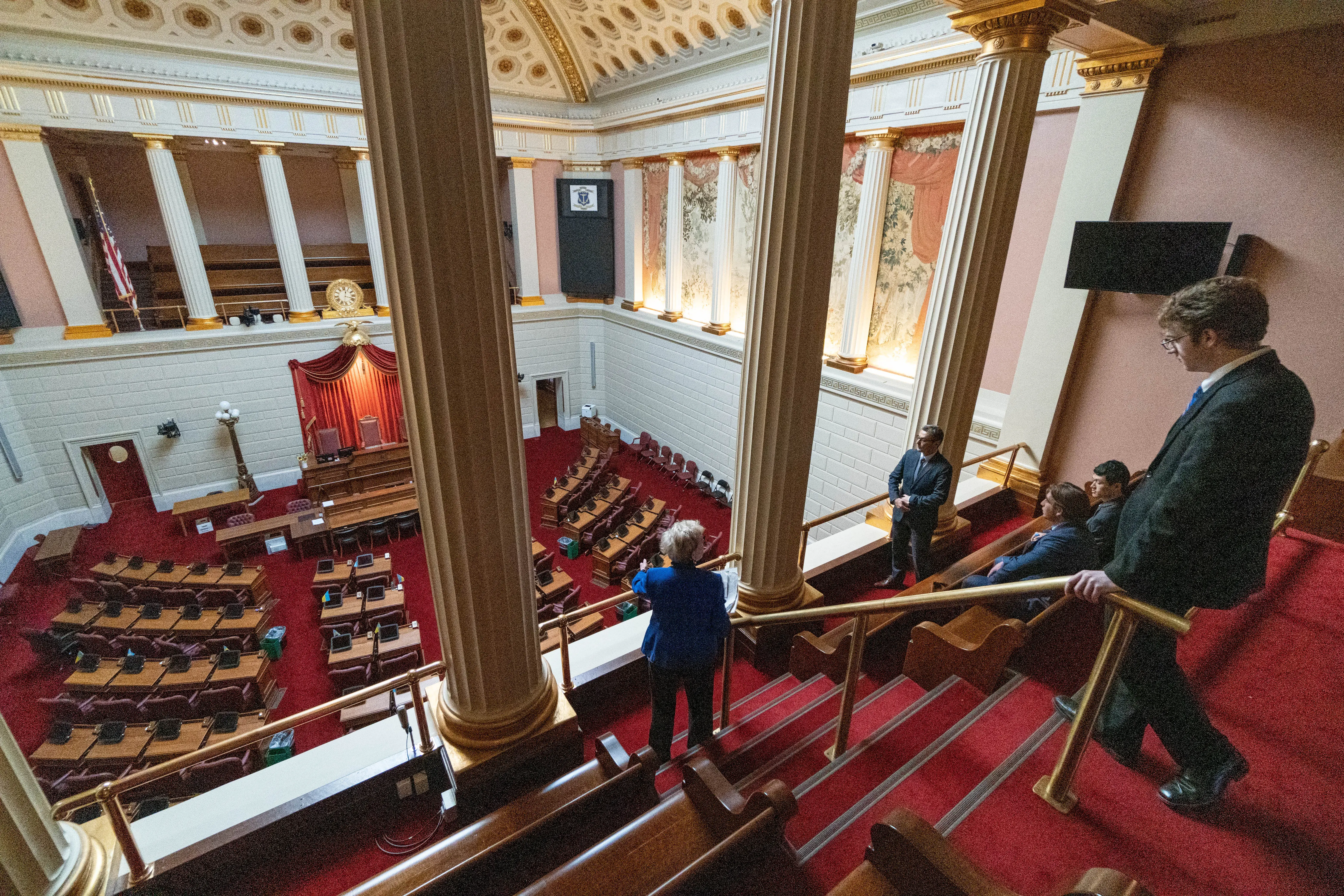 People observe a government chamber from a balcony inside a grand, column-lined legislative building.