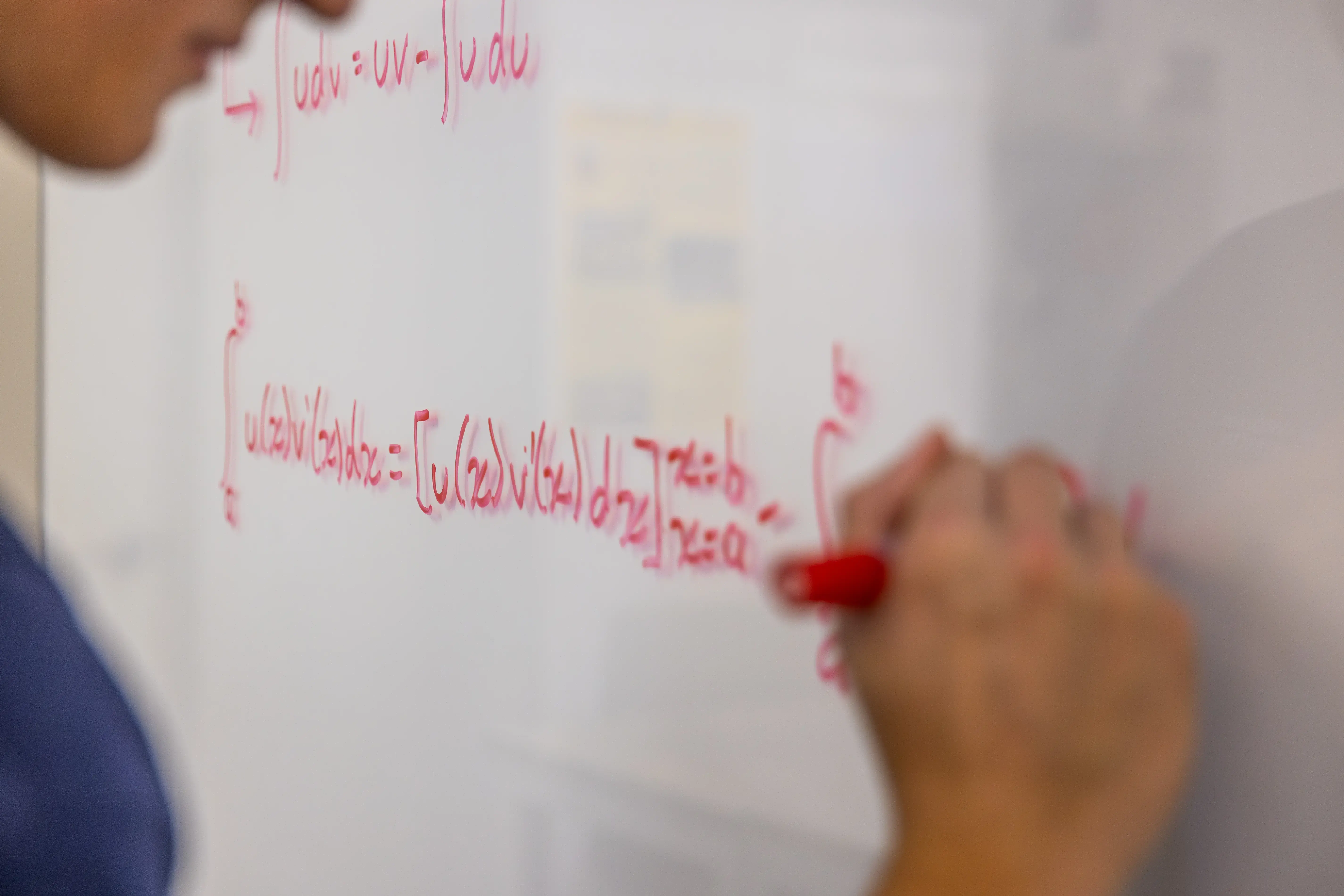 A person writes a complex integral equation with a red marker on a whiteboard, focusing on a math or calculus problem.