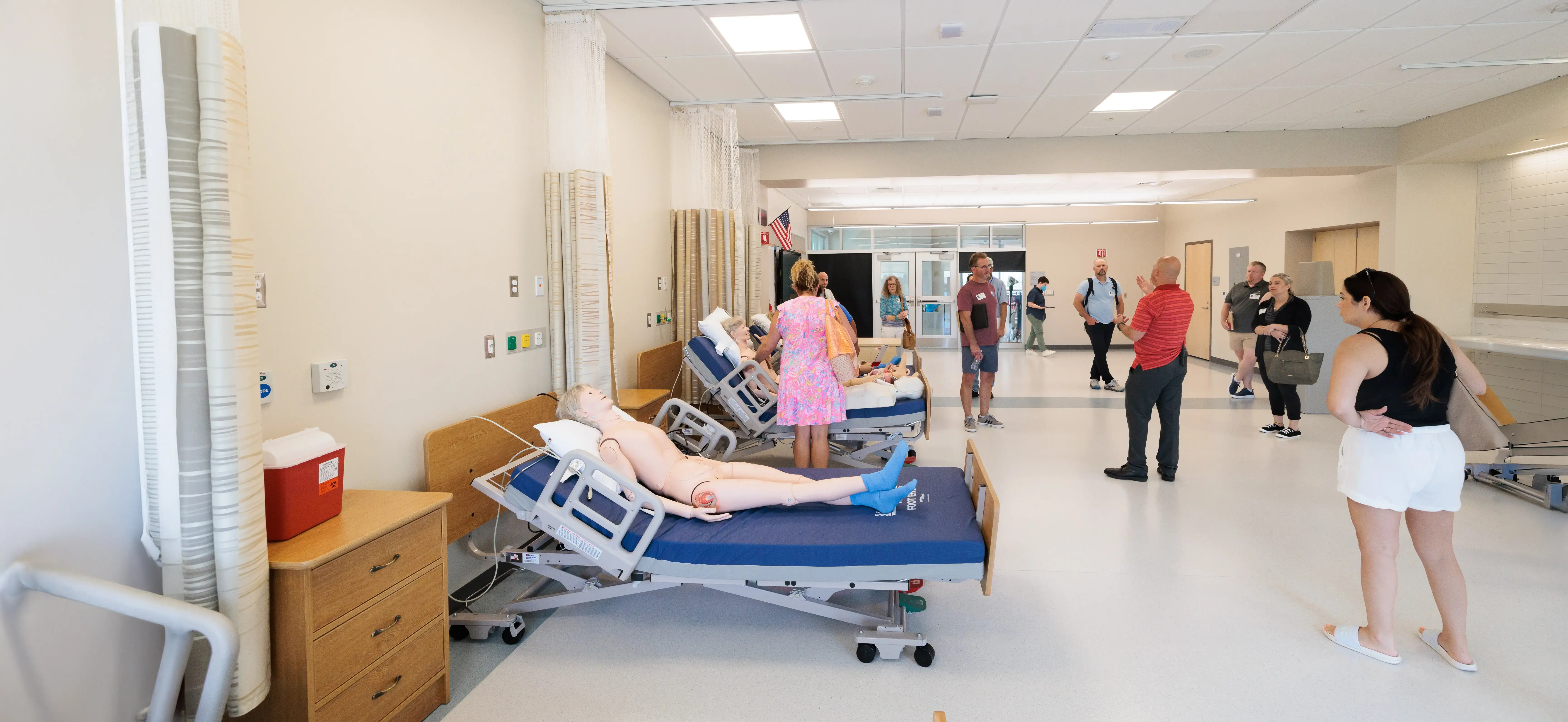 People tour a clinical simulation lab with hospital beds, observing the training environment for healthcare students.