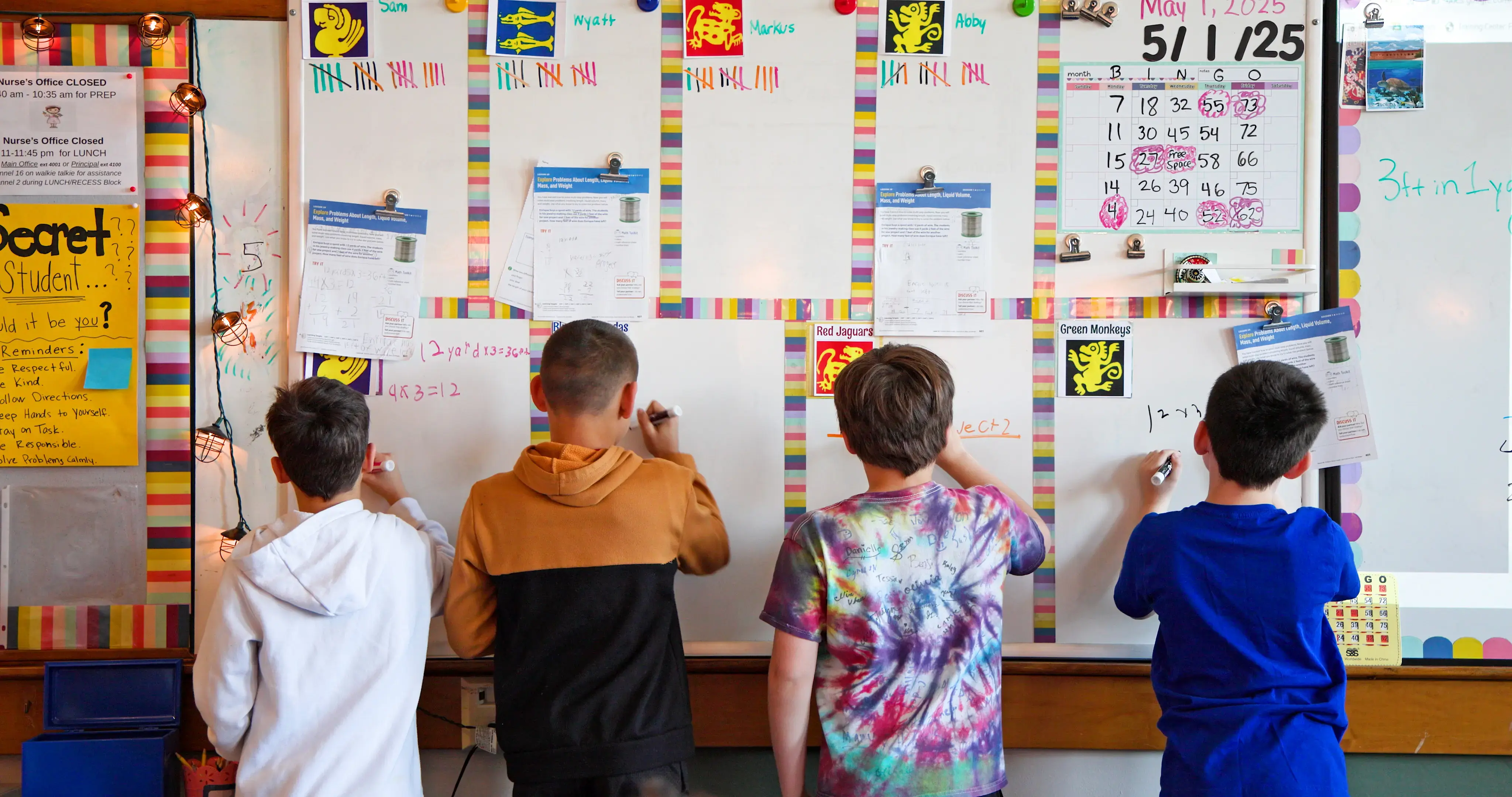 Children line up to complete math problems on a whiteboard