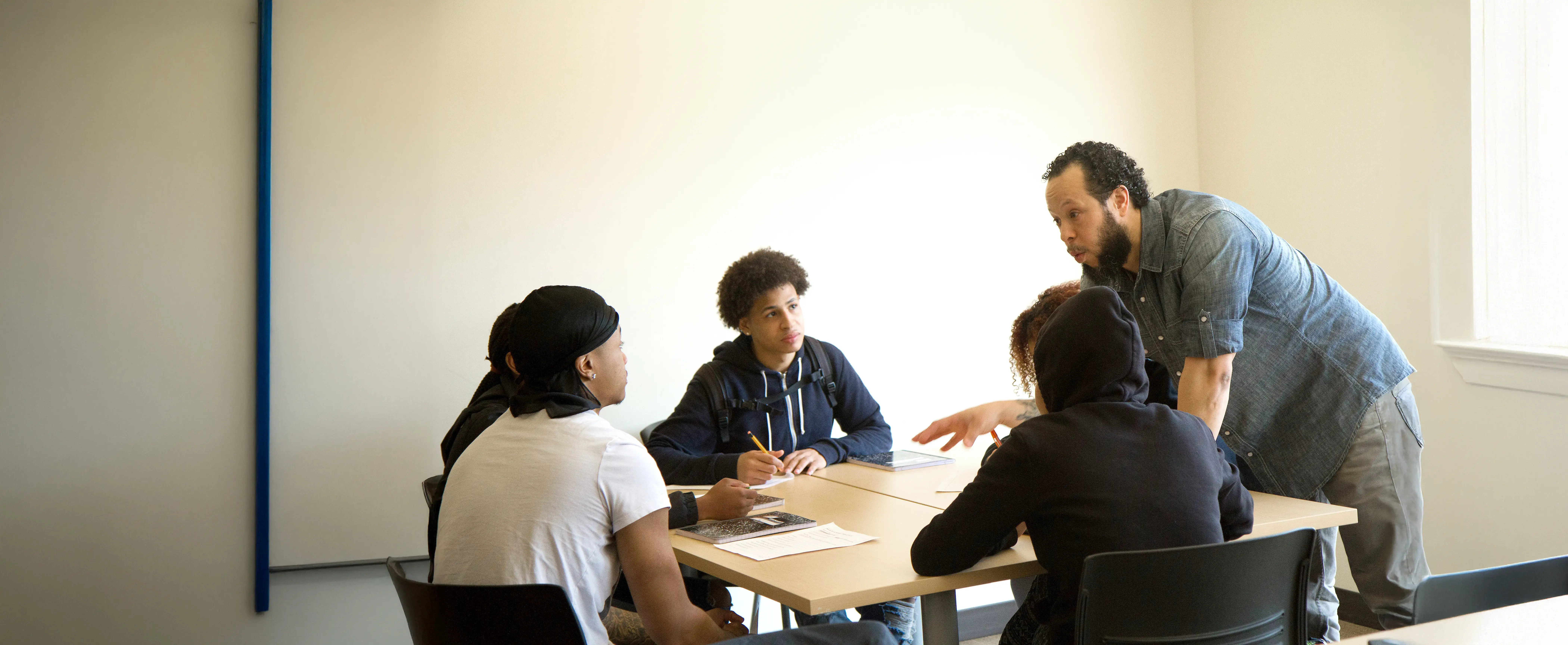 A high school teacher works with students in a classroom setting.