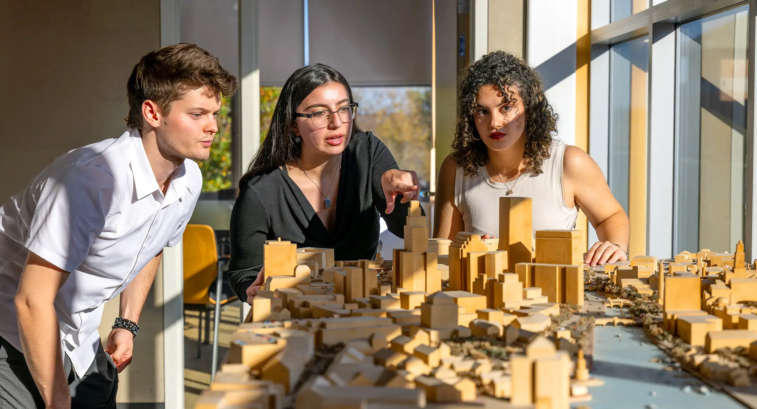 Architecture students look over a wooden model of a city