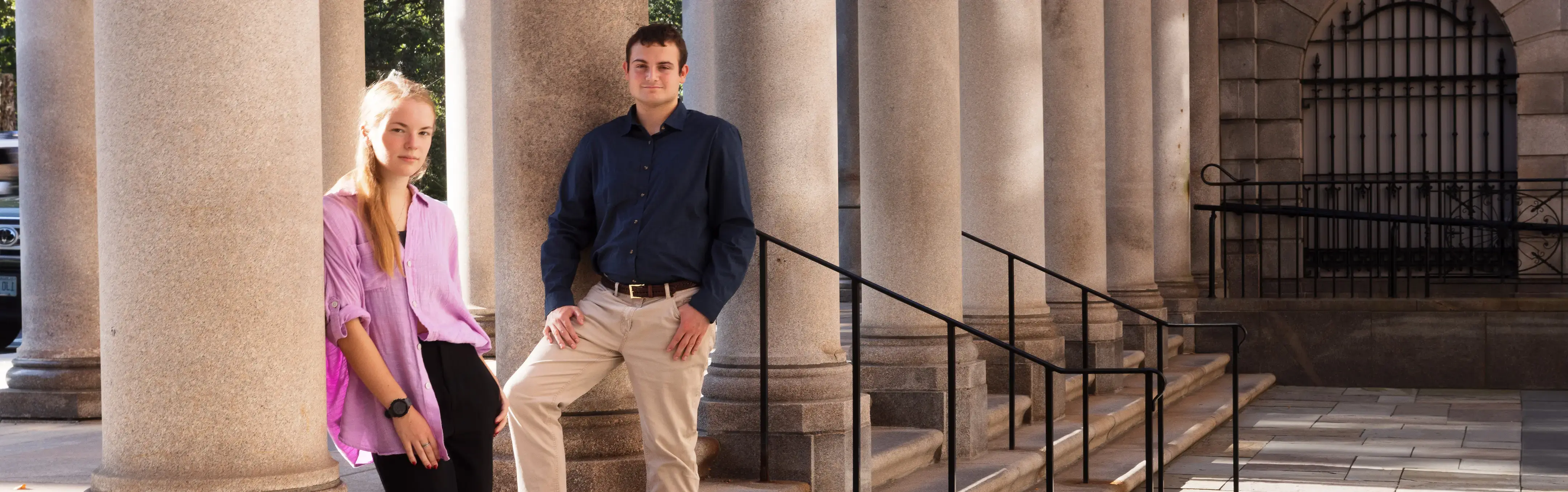 Grad students stand outside a courthouse leaning against granite columns