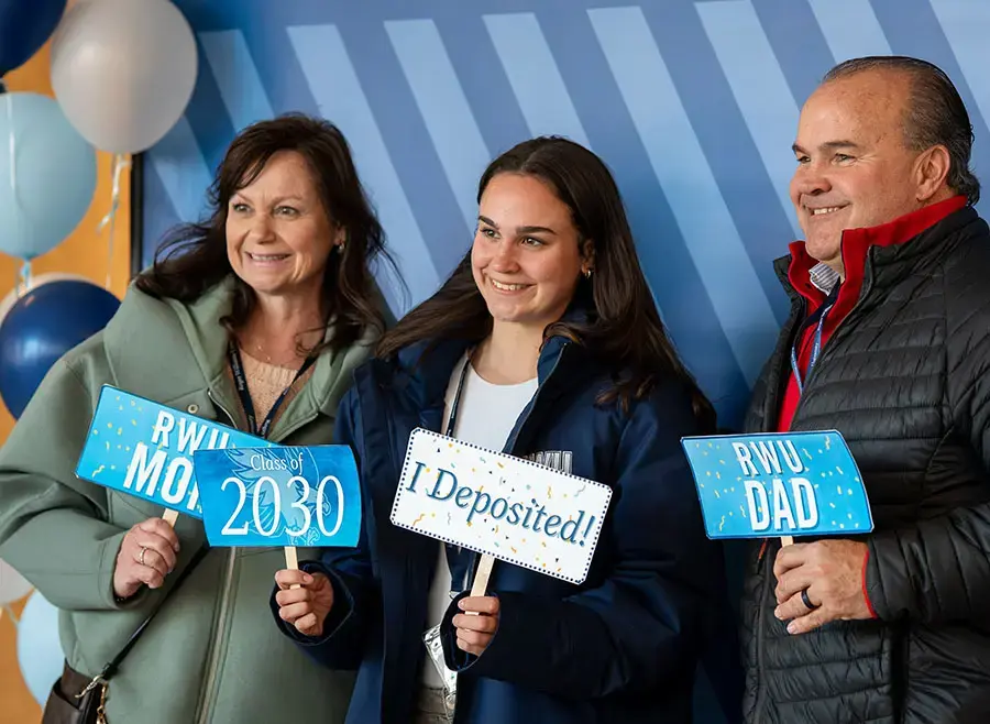 Student stands with their parents holding signs celebrating their deposit